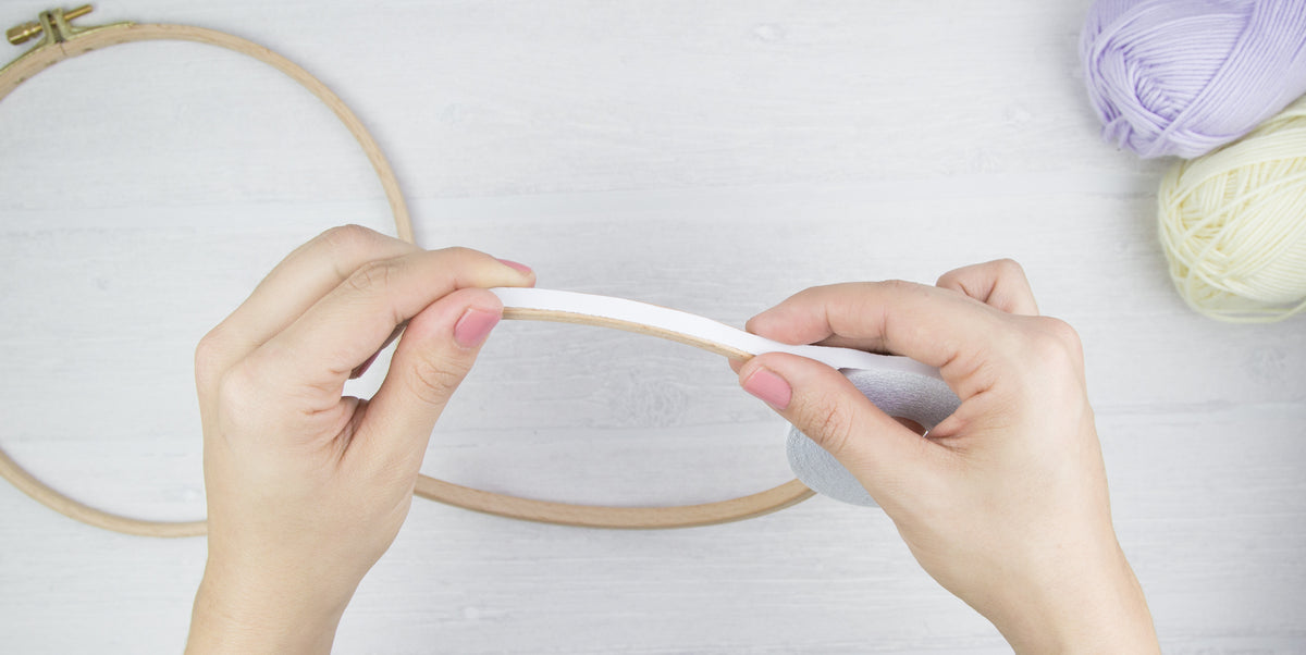 Klebeband wird auf den inneren Ring eines Holzstickrahmens aufgeklebt.