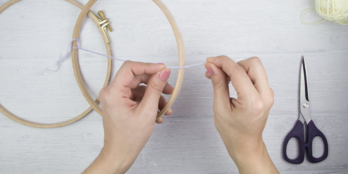 Ein Wollfaden wird am inneren Ring eines Stickrahmens befestigt.