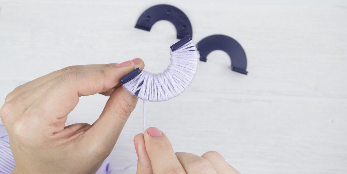 Ein Pompon Maker wird mit helllila Wolle umwickelt.