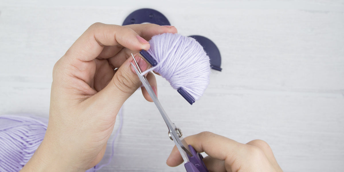 Der überschüssige Wollfaden an einem vollständig umwickelten Pompon Maker wird abgeschnitten.