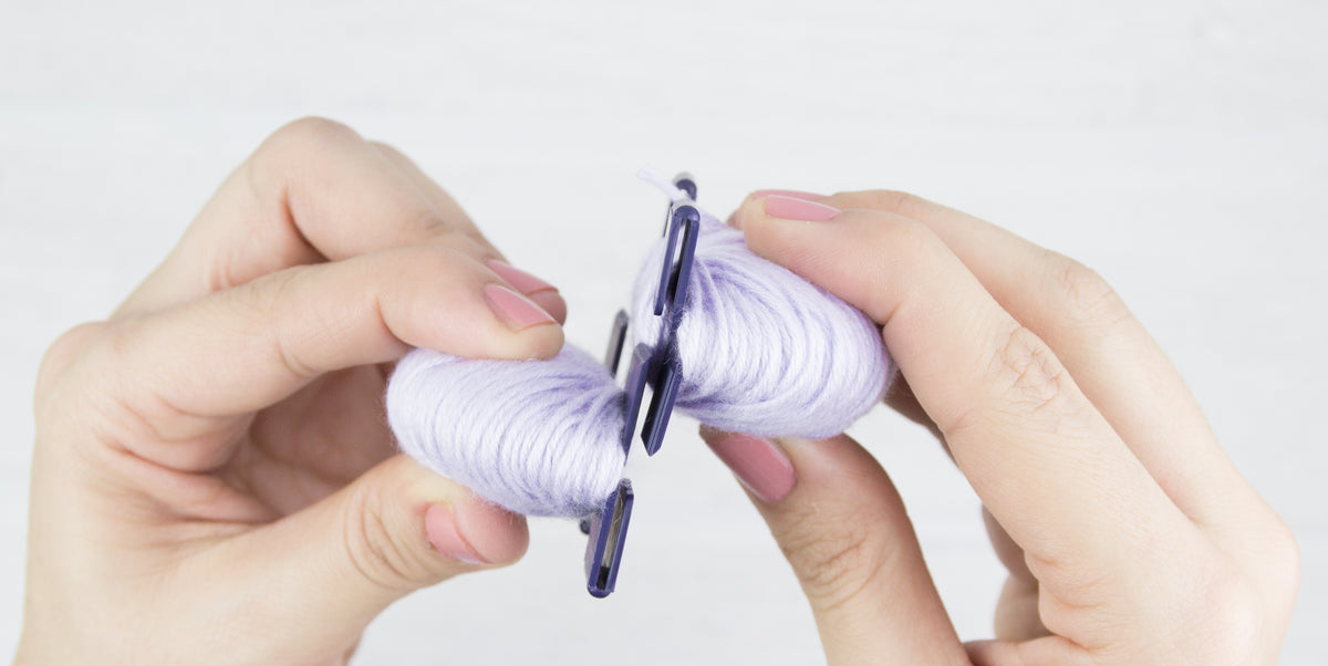 Zwei mit Wolle umwickelte Pompon-Schablonen werden zu einer runden Form zusammengesteckt.