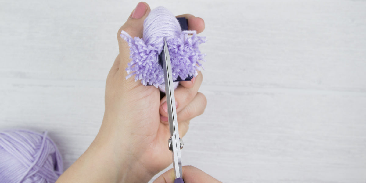 Pompon aufschneiden: Die umwickelten Wollfäden werden entlang der Außenseite des Prym Pompon Makers durchgeschnitten, um die charakteristische Pomponform zu erzeugen.
